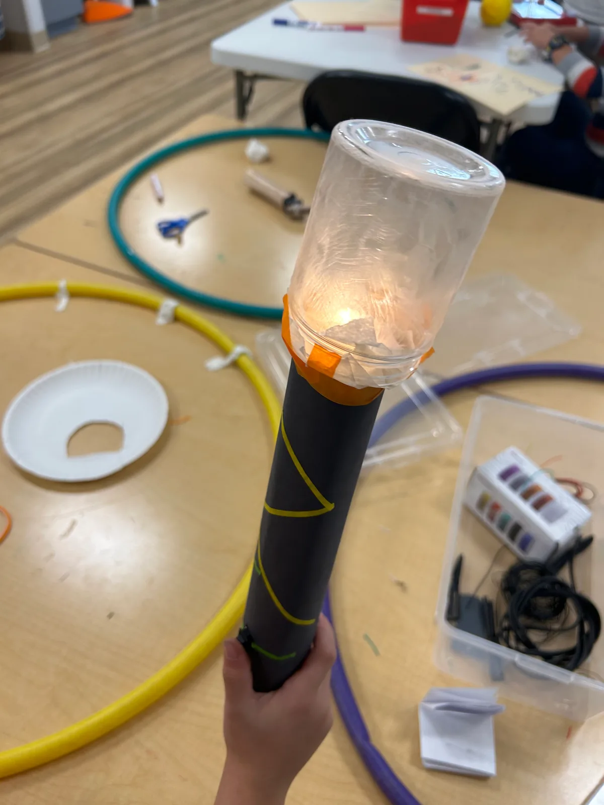 A lantern from a cardboard tube and a plastic jar, lit by a salvaged bulb