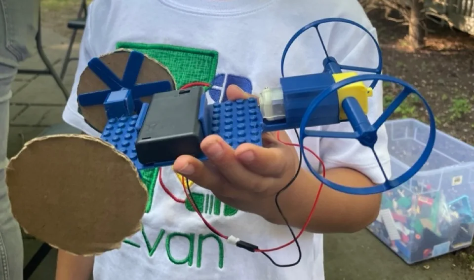 A finished car in a participant's hands: printed chassis and hubs, cardboard wheels, motor and battery pack